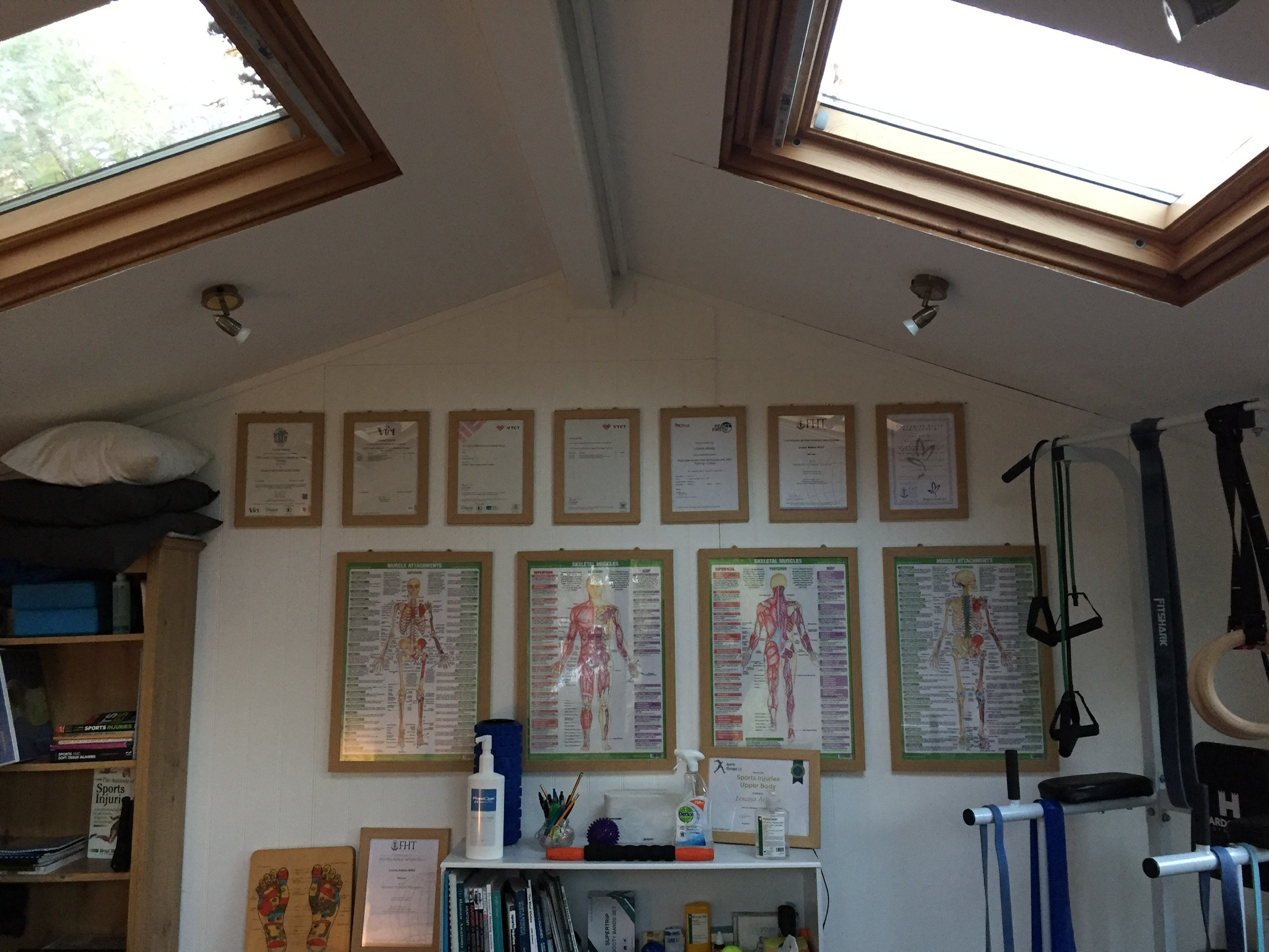 Inside the studio: two skylights, a row of framed certificates and four anatomy charts on the wall, treatment kit on the shelf below.