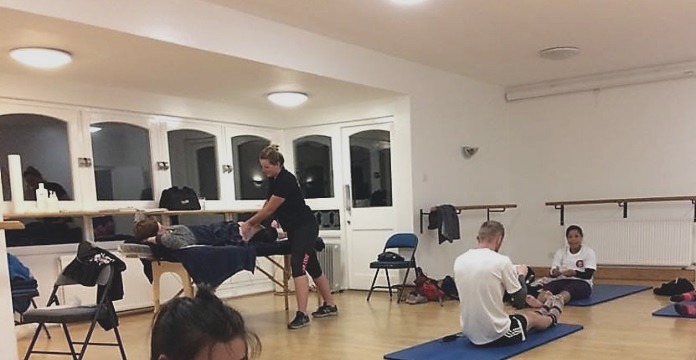 Louisa treating in a hall while a group stretches on mats.