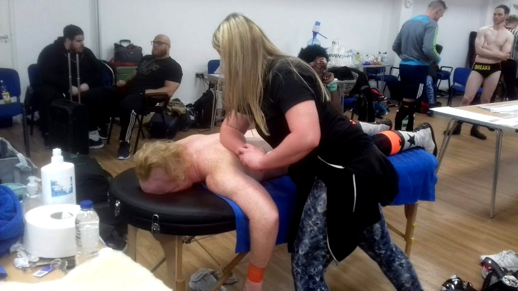 Louisa treating a wrestler on a massage couch backstage at an event.